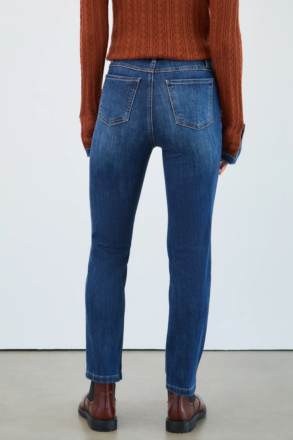 Person wearing blue jeans and a brown sweater against a white background