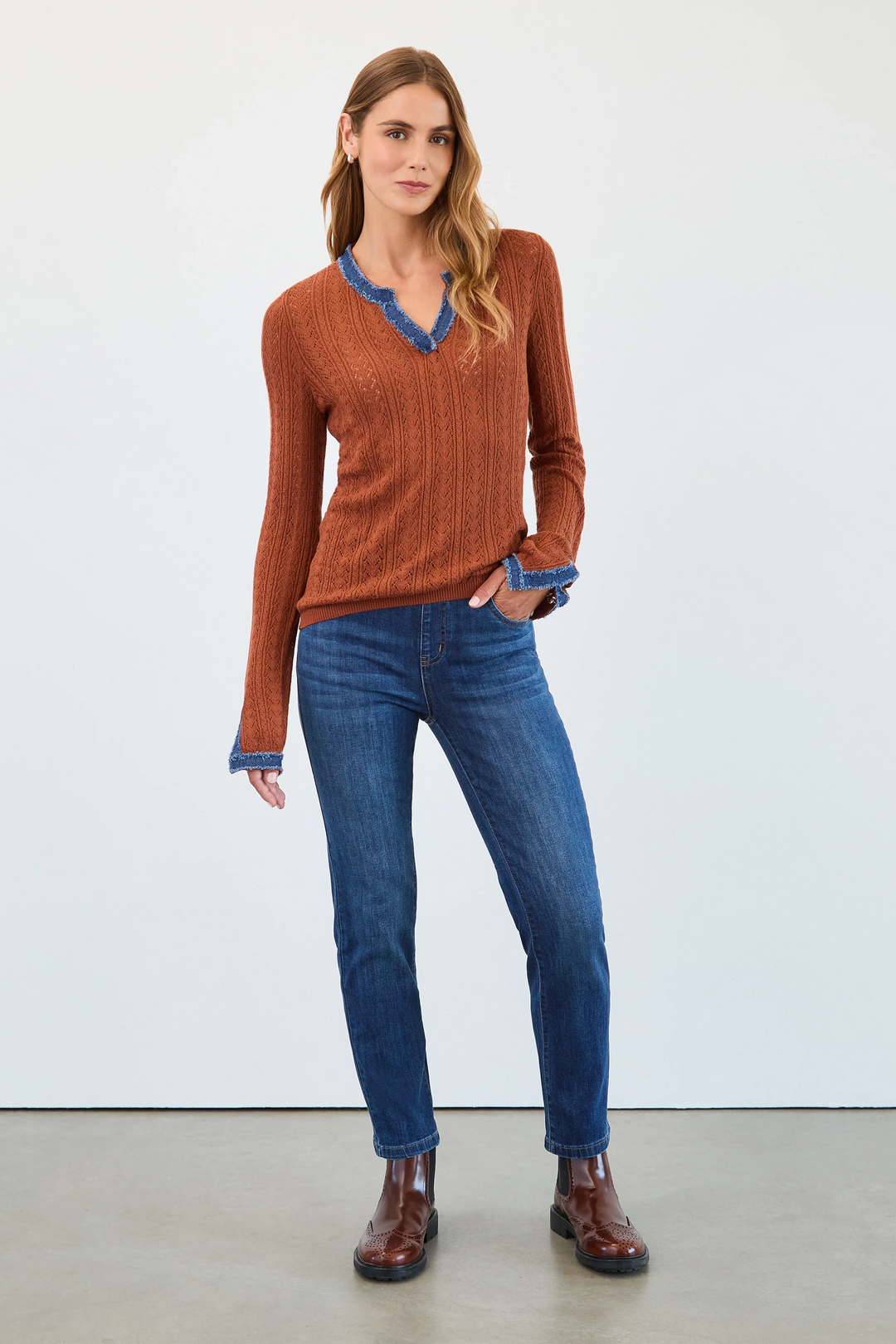 Woman wearing a brown sweater with blue trim, blue jeans, and brown shoes on a white background