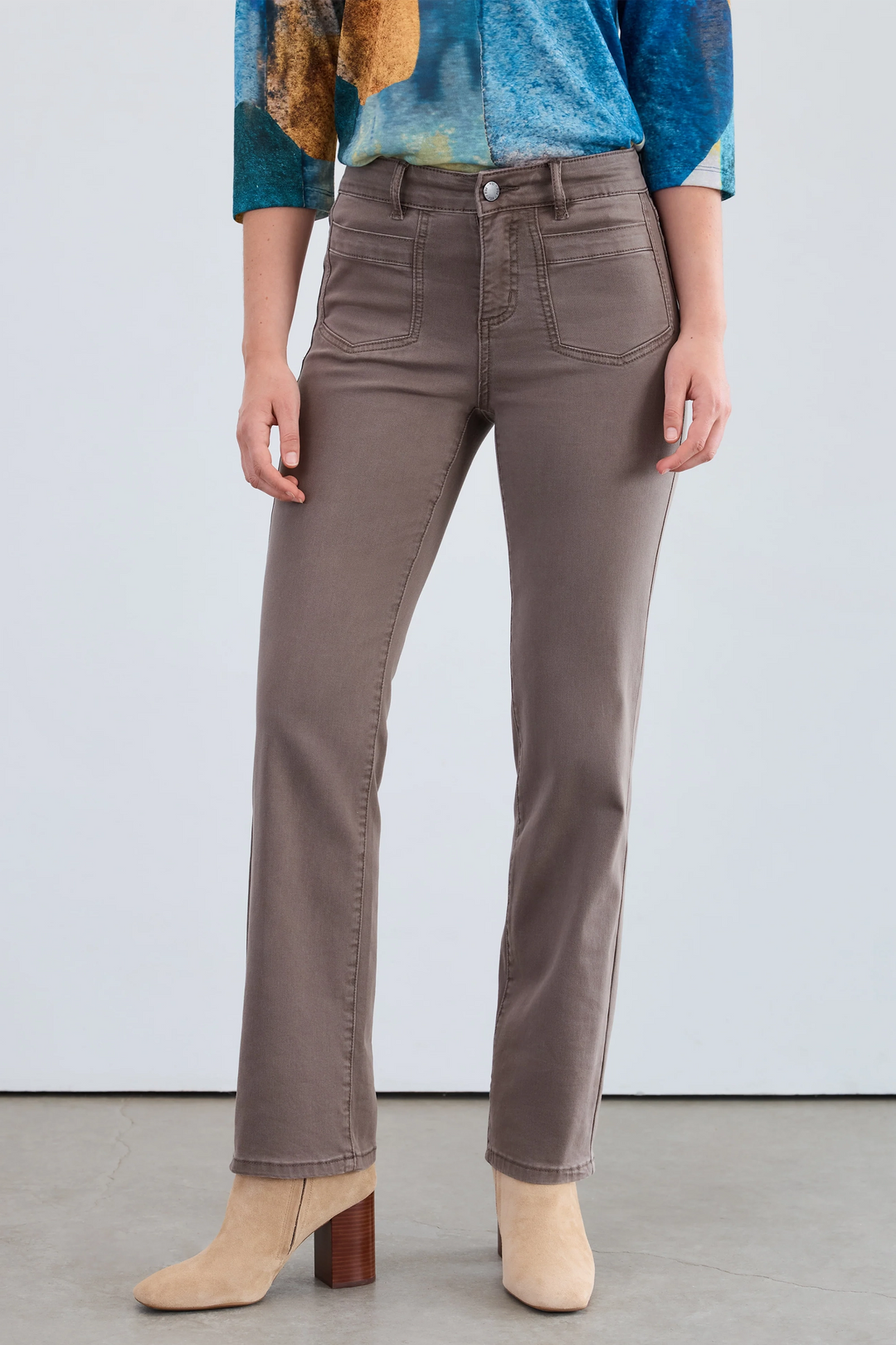 Person wearing brown straight-leg jeans with a colorful top and beige boots on a plain background