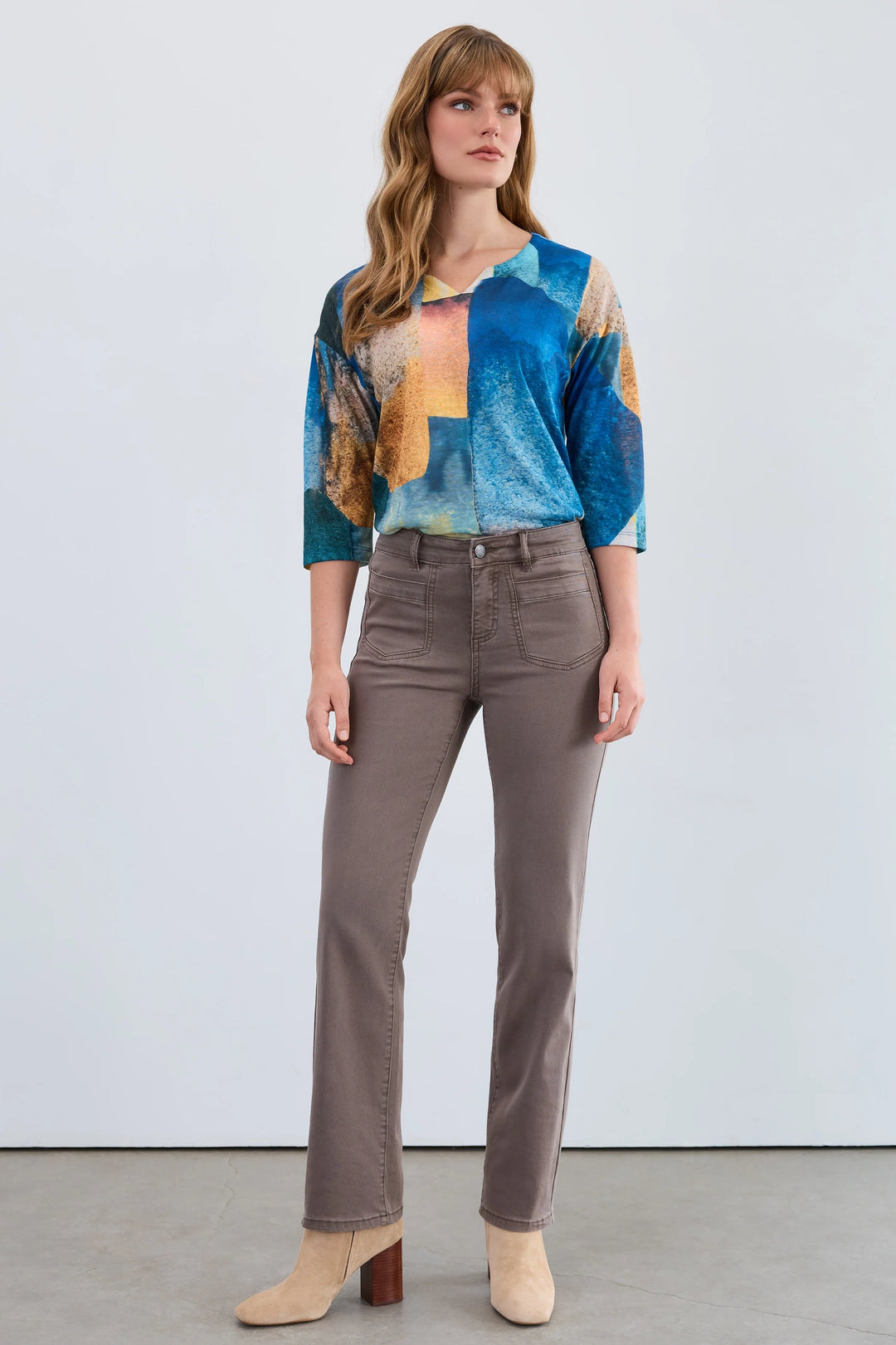 Woman wearing a colorful top and brown pants against a white background