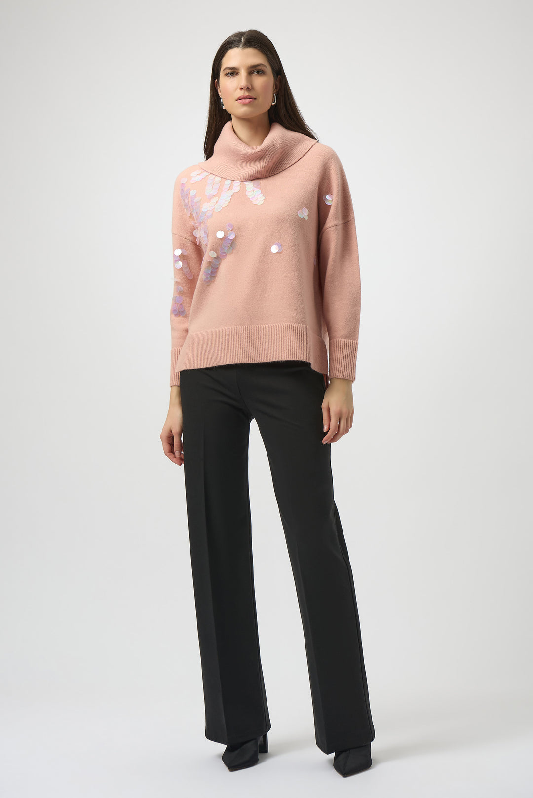 Woman wearing a pink sweater with floral patterns and black dress pants on a white background