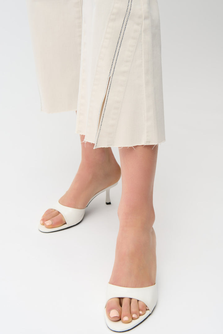 White high-heeled sandals worn with a light-colored capri pant on a white background