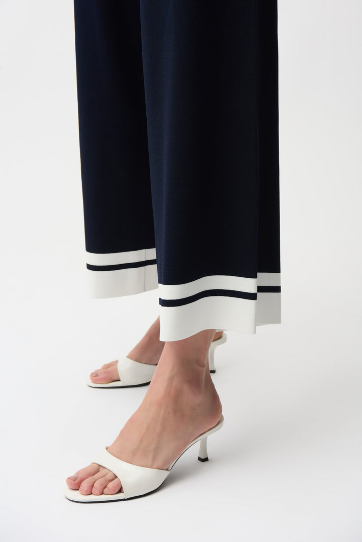 White high-heeled shoes worn with navy wide leg pants on a white background
