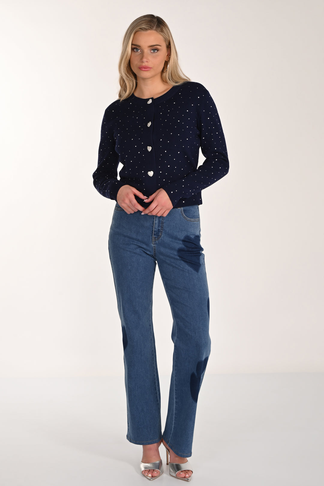Woman wearing a navy blue cardigan with white buttons and blue jeans with hearts on a white background