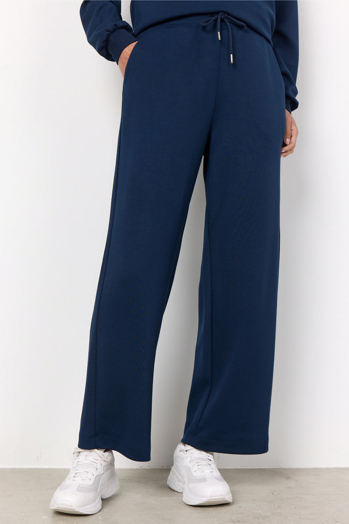 Person wearing navy blue pants and white sneakers on a plain background