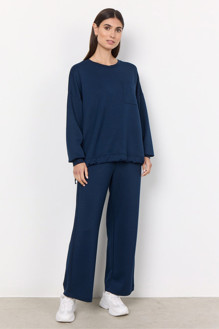 Woman wearing a navy blue outfit with white sneakers on a plain background