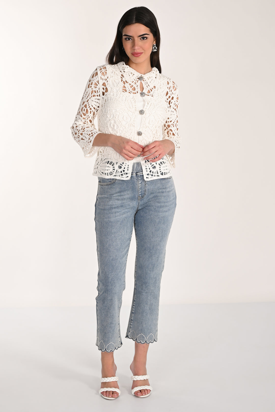 Woman wearing a white lace top and light blue jeans on a white background