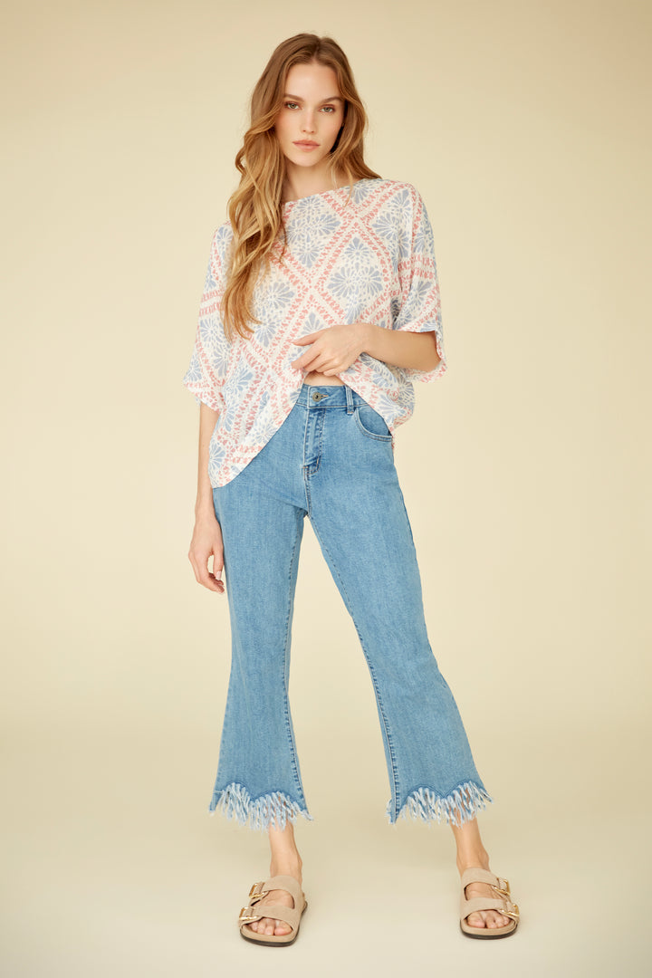 Woman wearing a patterned top and blue jeans on a beige background