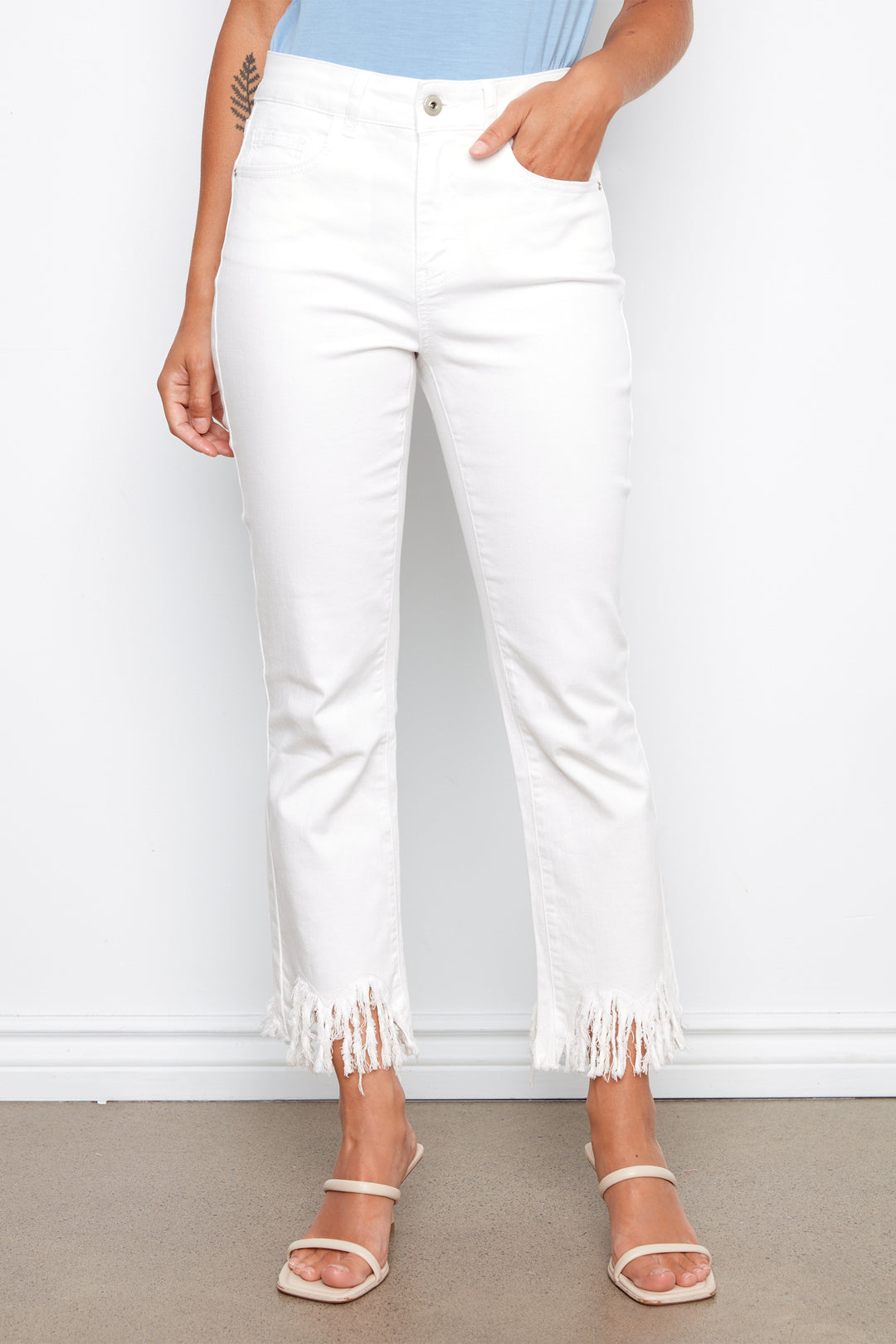 Person wearing white pants with fringe details on a plain background