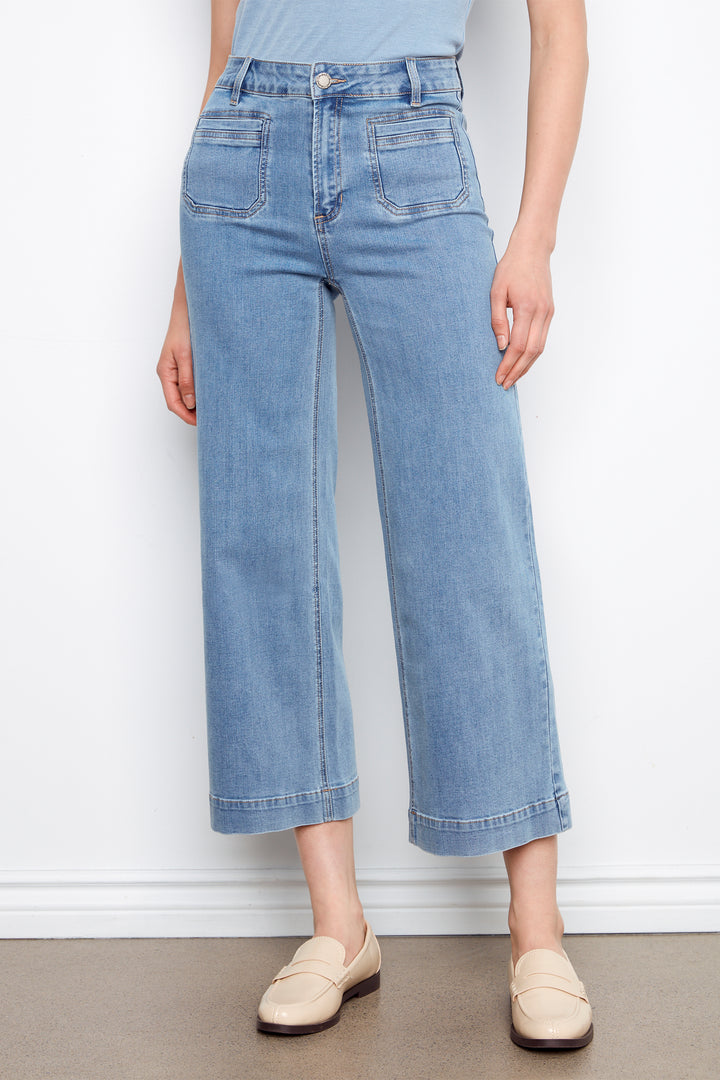 Person wearing light blue jeans and white shoes on a plain background