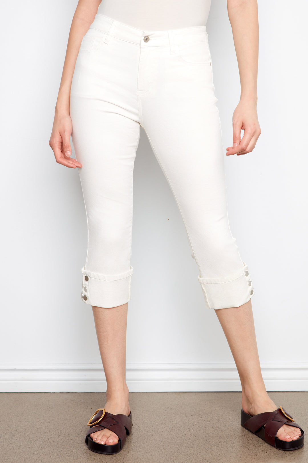 Person wearing white capri pants with button details on a plain background