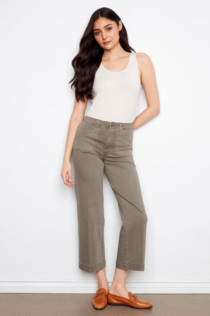 Woman wearing a white tank top and green pants against a white background