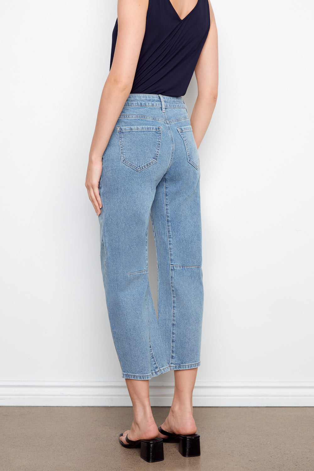 Person wearing blue jeans and a navy top against a white wall.