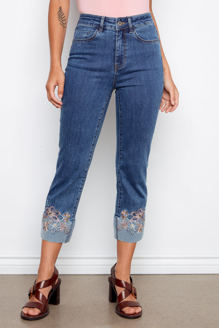 Person wearing blue jeans with floral embroidery at the cuffs against a white background