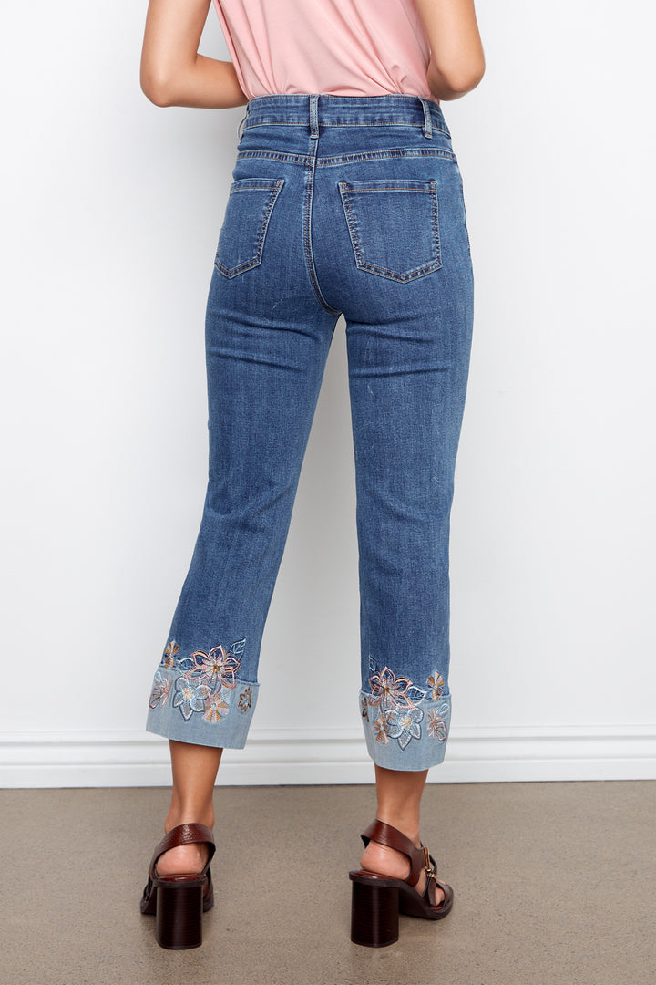 Person wearing blue jeans with floral embroidery at the cuffs on a plain background