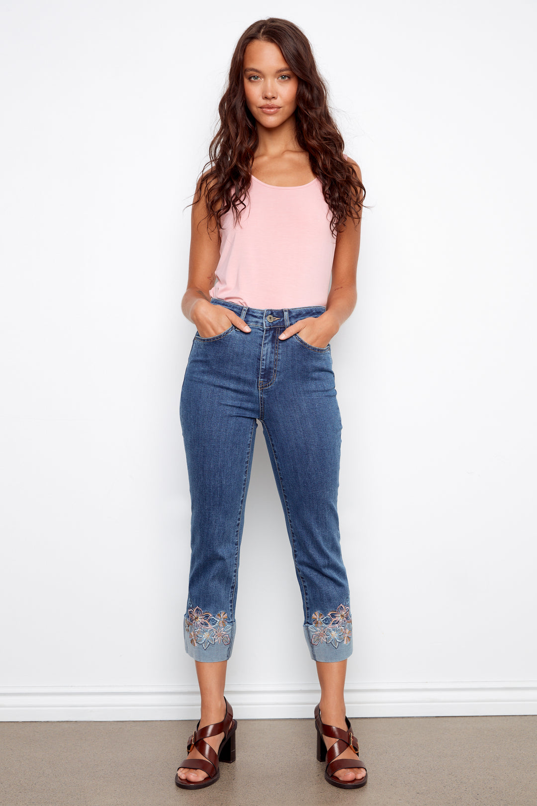 Woman wearing a pink top and blue jeans with embroidered cuffs against a white background