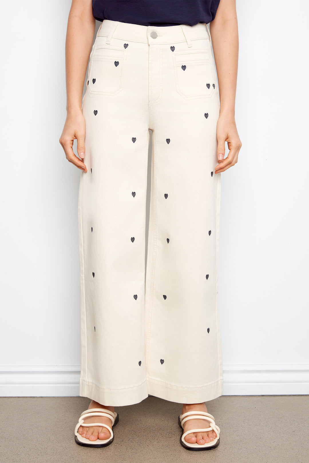 White wide-leg pants with black heart patterns worn by a person on a plain background