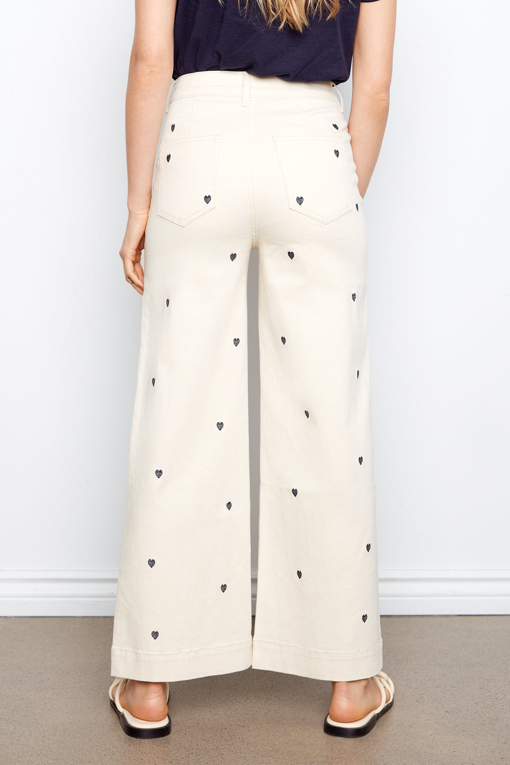 White pants with black heart patterns worn by a person against a plain background