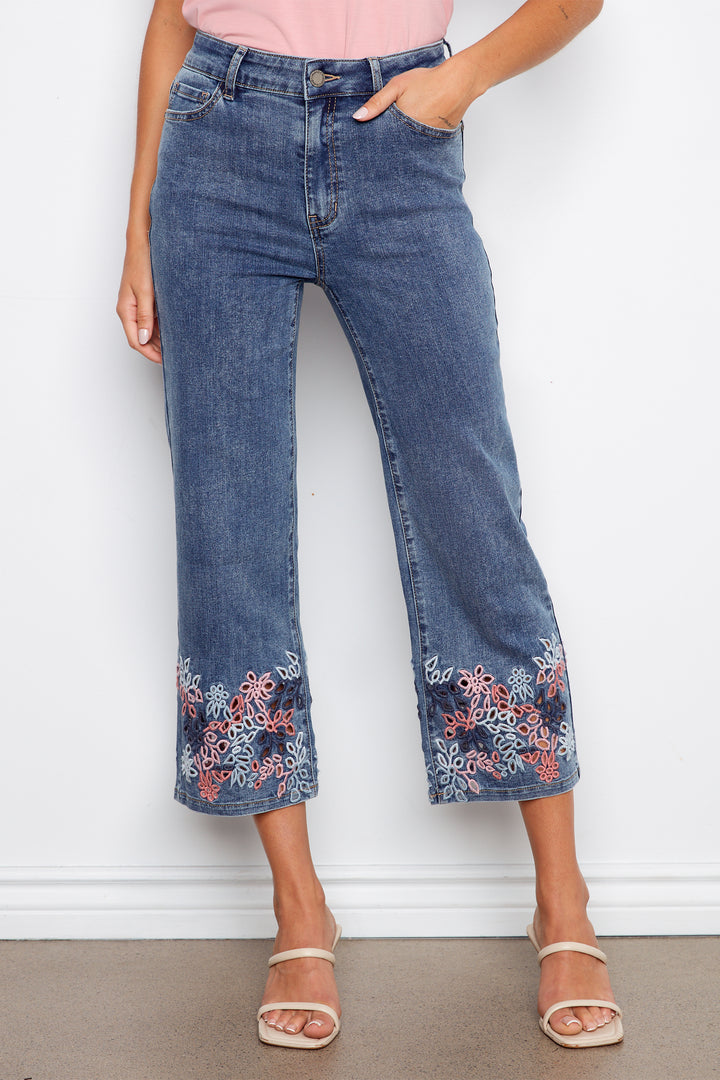 Person wearing blue jeans with floral embroidery on a white background