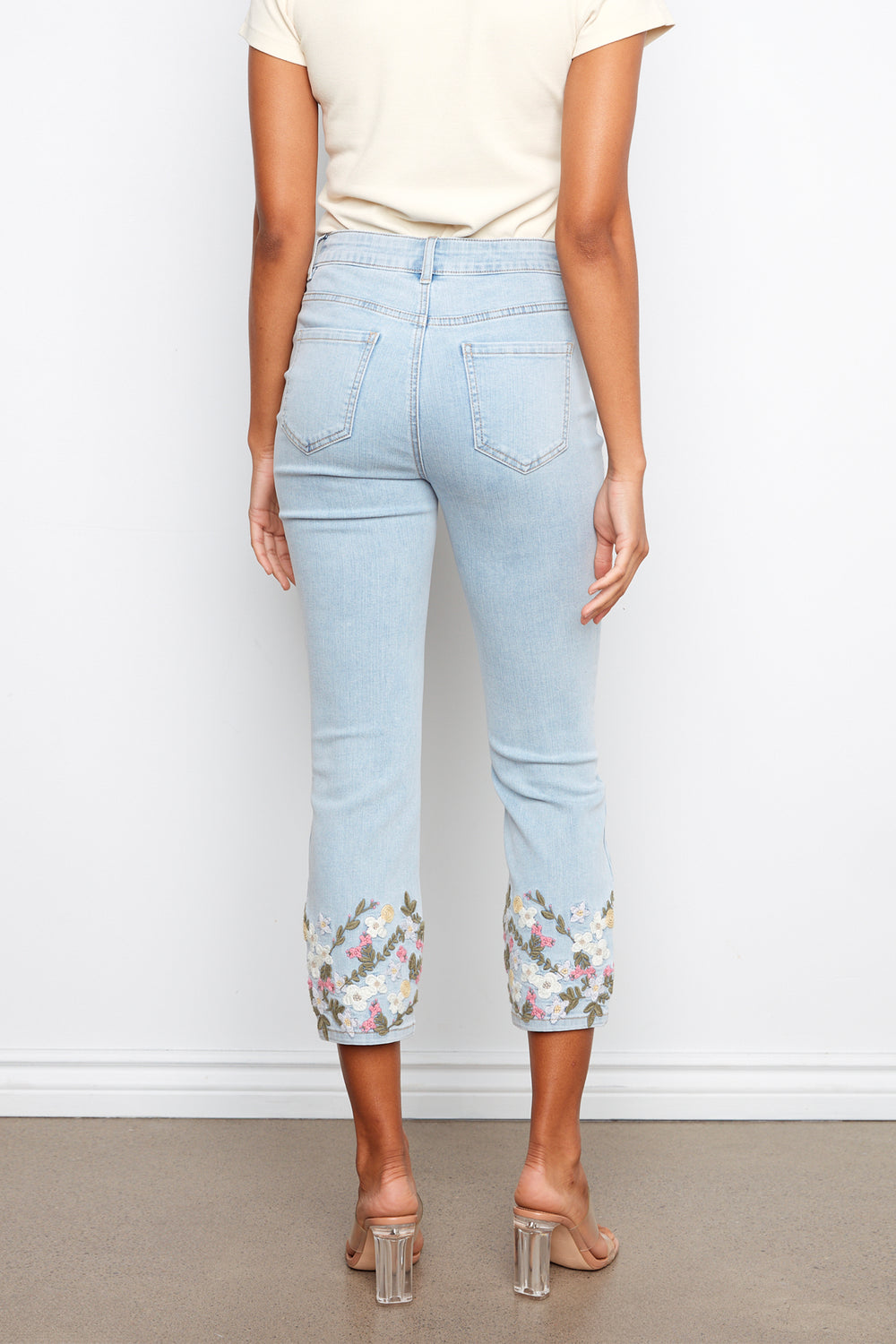 Light blue jeans with floral cuffs worn by a person against a white background
