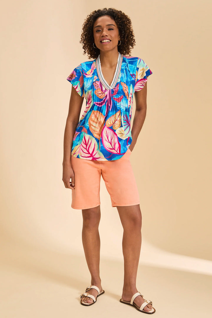 Woman wearing a colorful tropical print top and peach shorts on a beige background