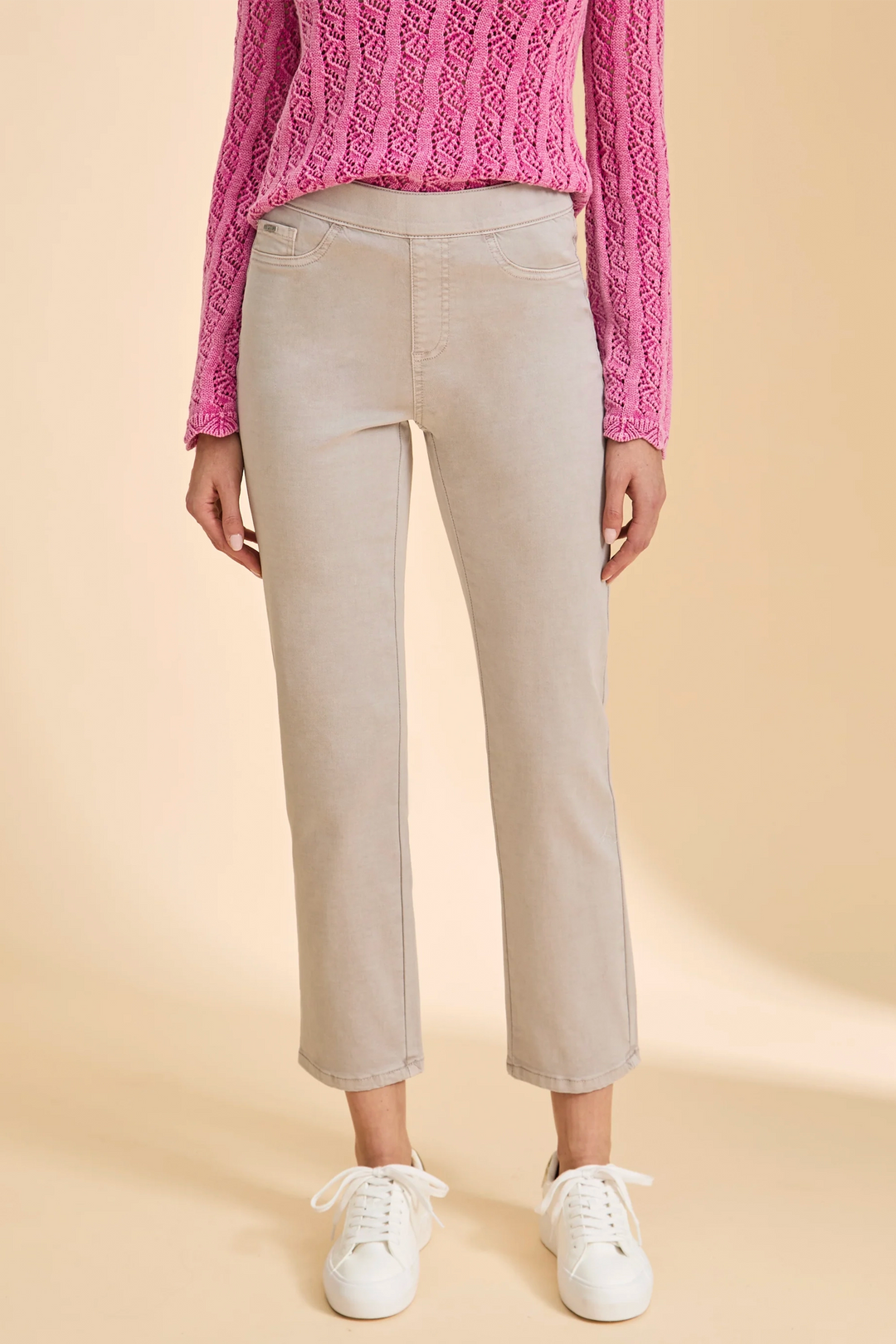 Person wearing beige pants and a pink knitted sweater on a beige background