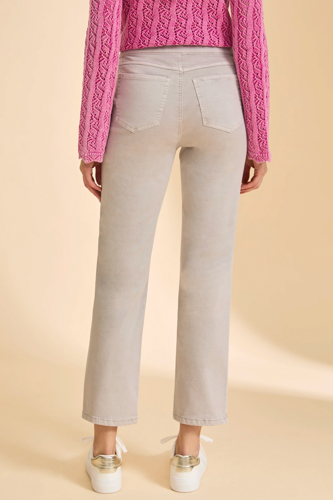 Person wearing light gray pants with a pink textured sweater on a beige background