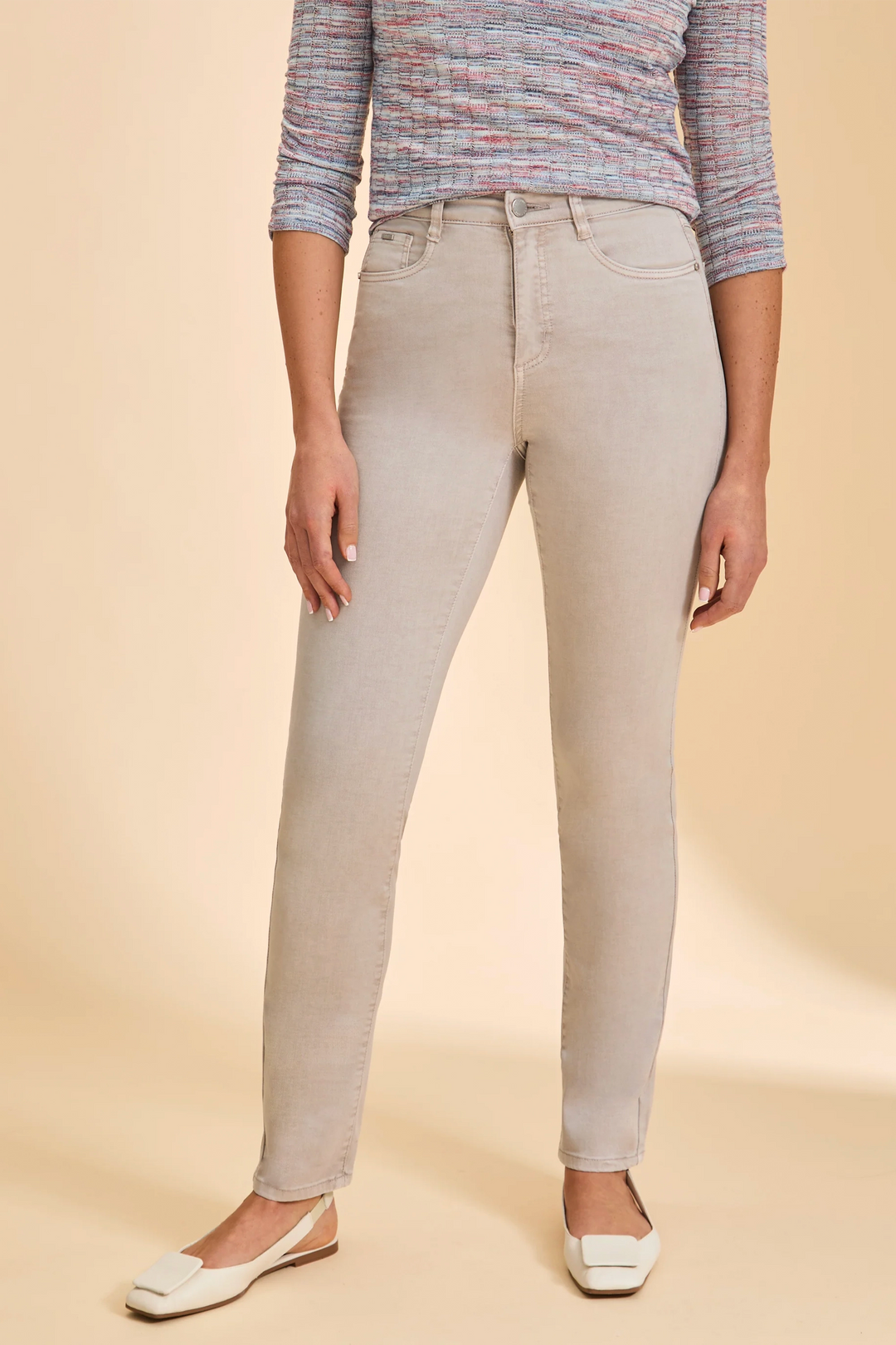 Person wearing beige pants and a multicolored top on a beige background