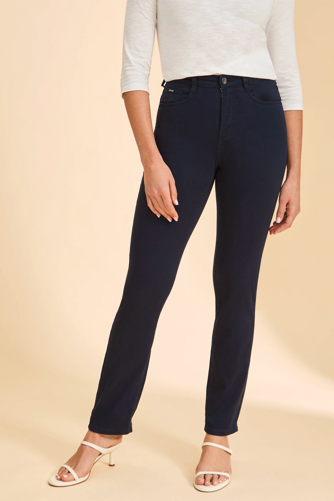 Person wearing navy blue jeans and a light gray top on a beige background