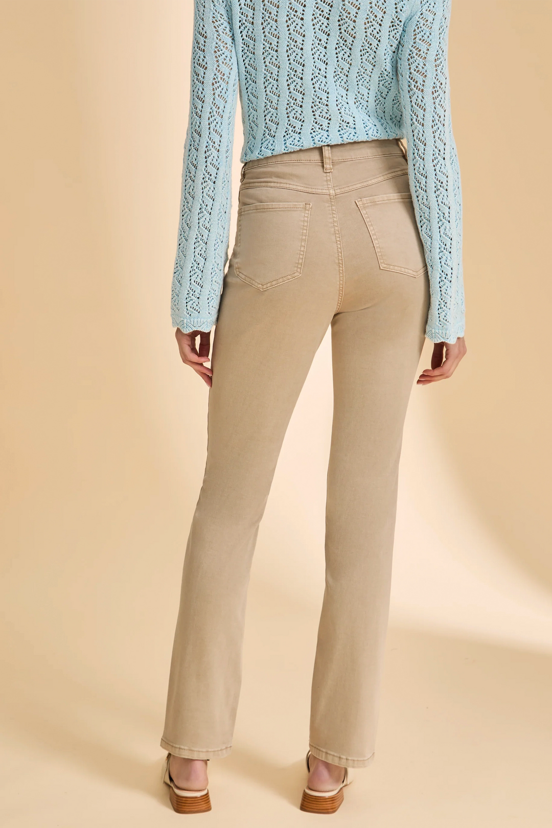 Person wearing a light blue knitted sweater and beige flared pants on a beige background