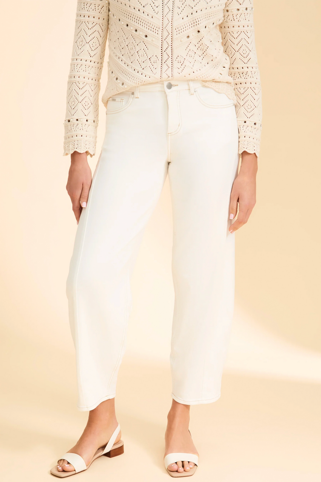 Person wearing a beige crochet top and white girlfriend jeans on a beige background