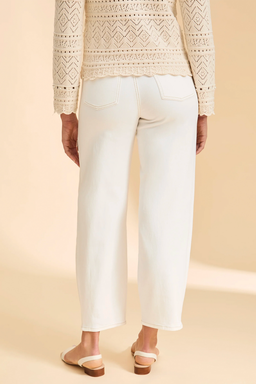 Person wearing a beige patterned sweater and white pants on a beige background