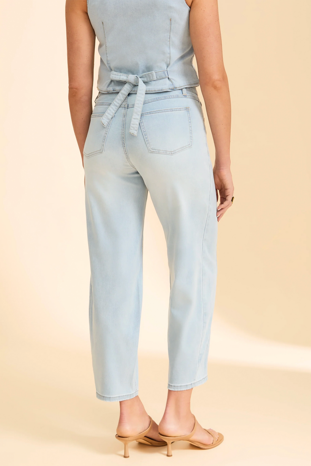 Light blue sleeveless top and jeans worn by a person on a beige background