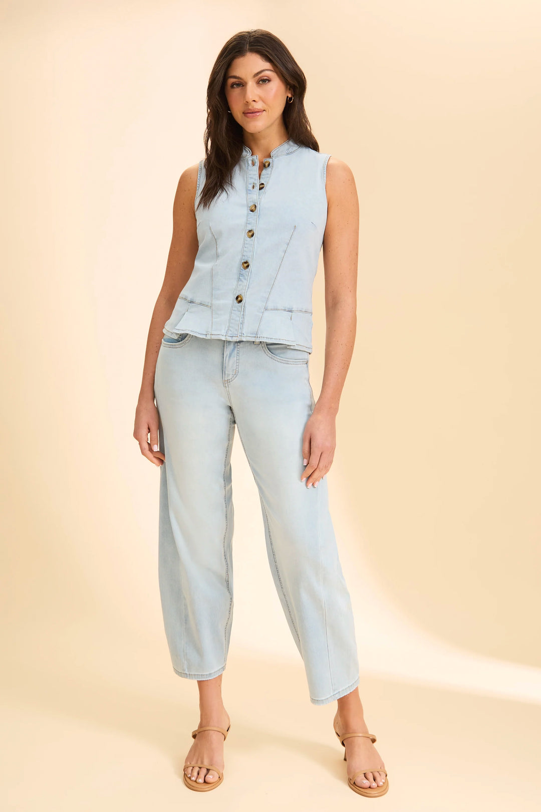 Woman wearing a light blue denim vest and jeans on a beige background