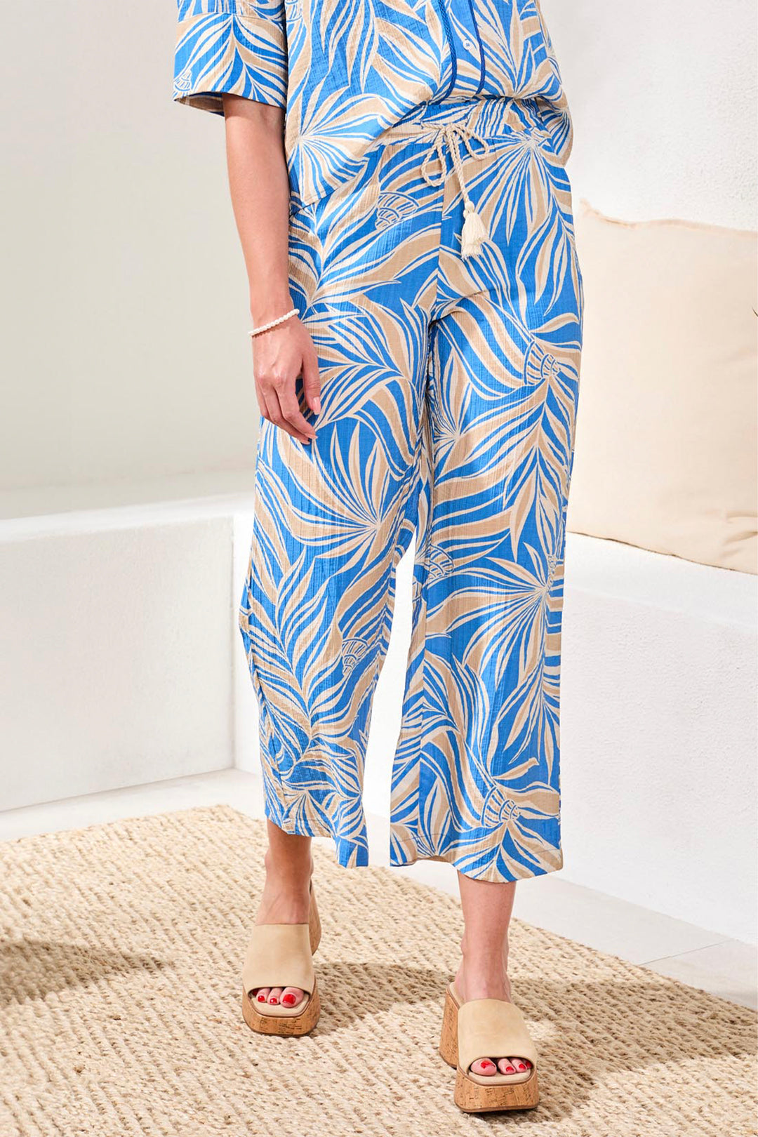 Person wearing a blue and white tropical wide-leg pants in a minimal indoor setting.