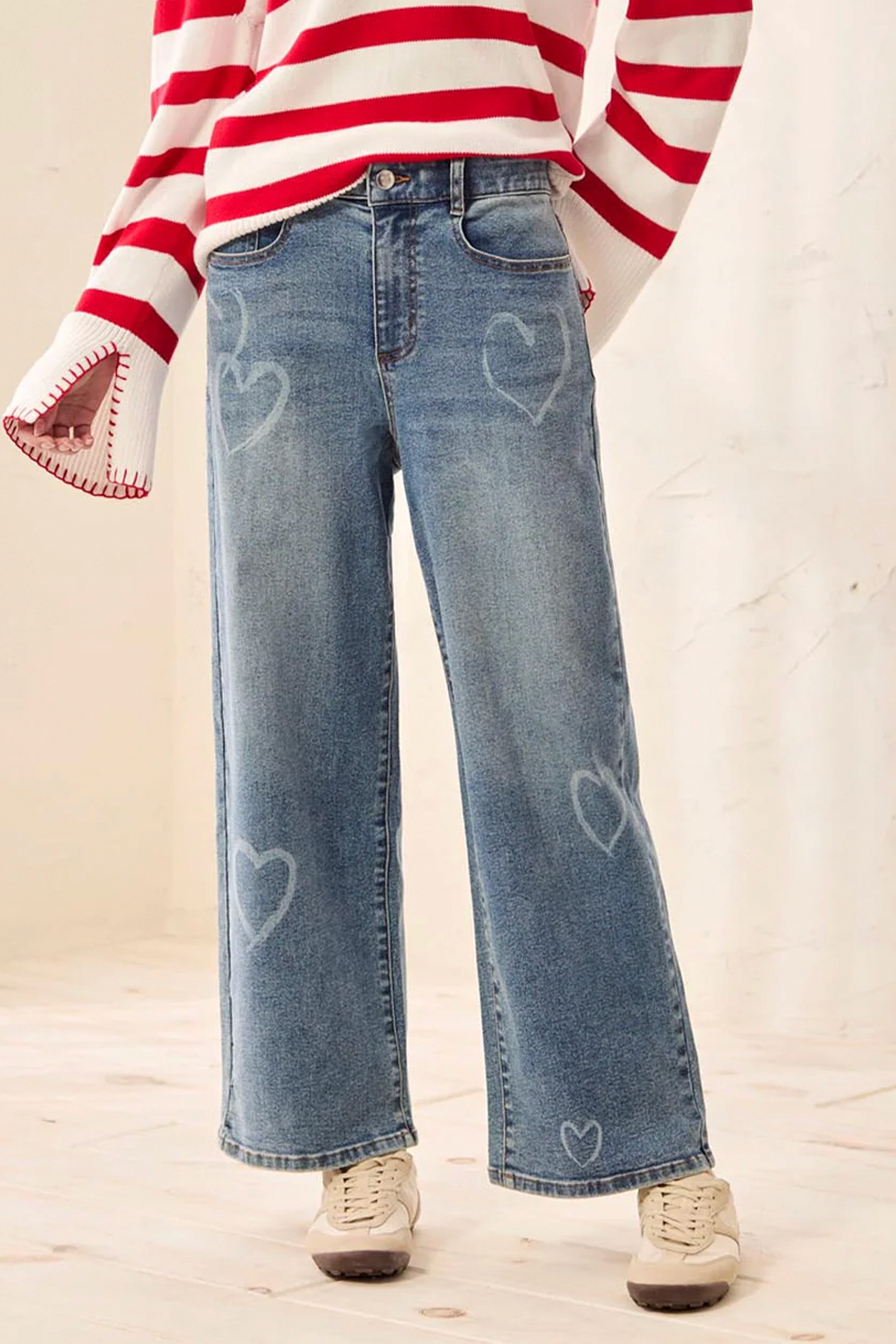 Person wearing red and white striped long-sleeve shirt with blue jeans featuring heart designs on a light background