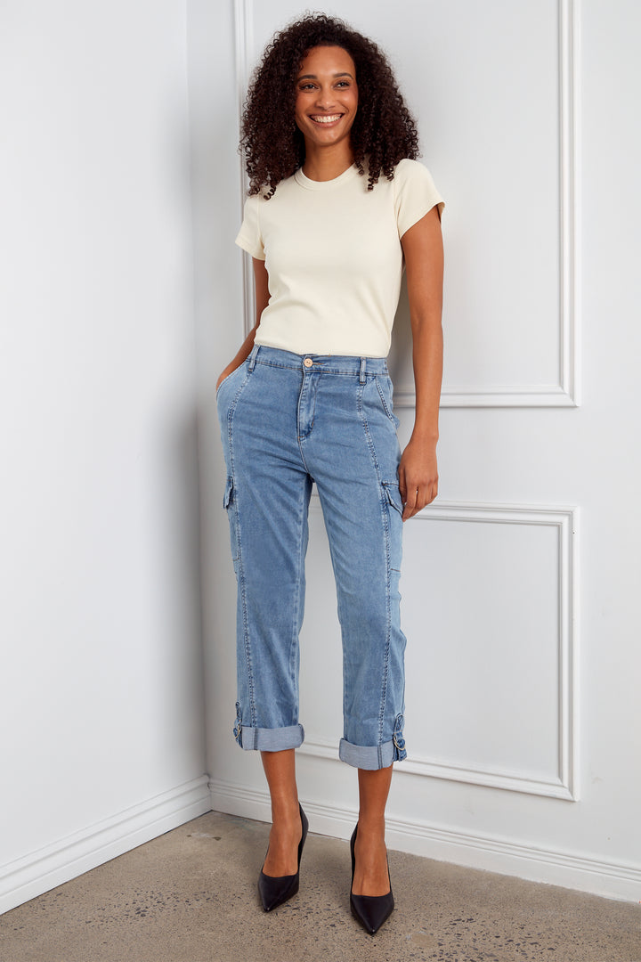 Woman wearing a white top and blue jeans standing against a white wall.