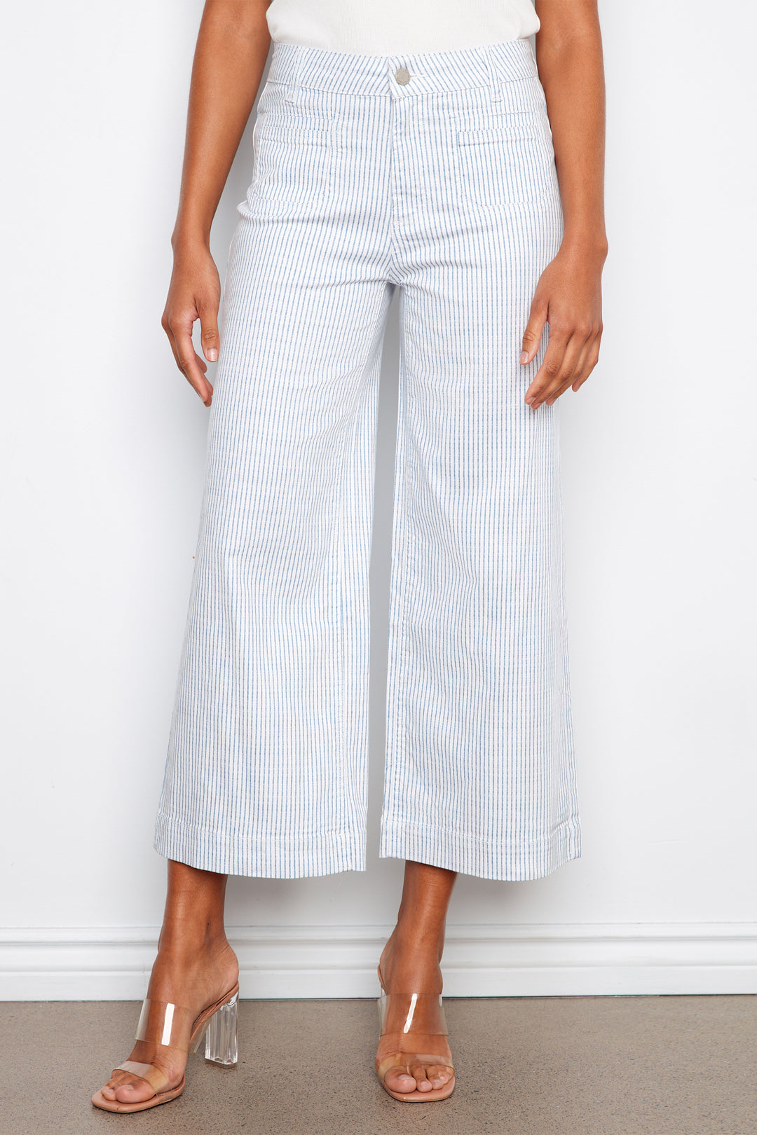 Person wearing white and blue striped wide-leg pants with clear heels on a plain background