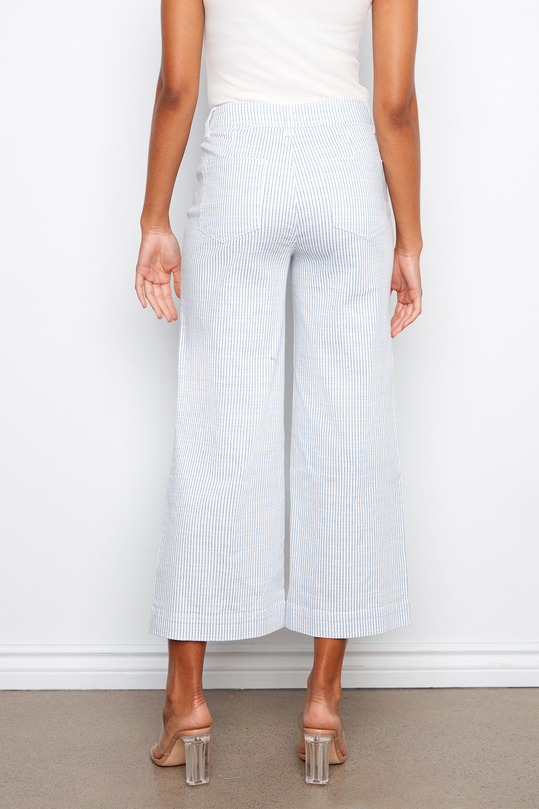 Person wearing light blue striped pants and clear high-heeled shoes on a plain background