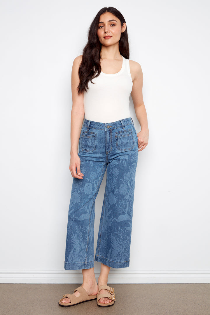 Woman wearing a white tank top and blue jeans against a white background