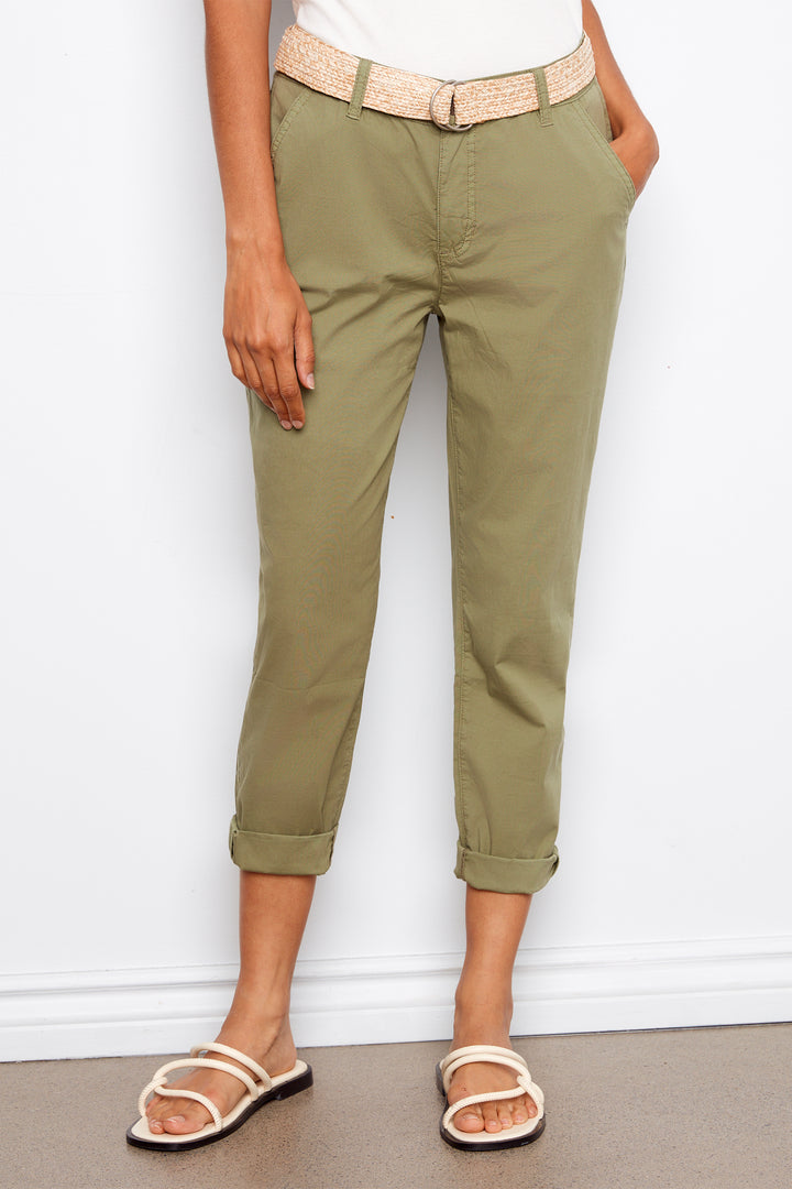 Person wearing olive green pants with a beige belt against a white wall.