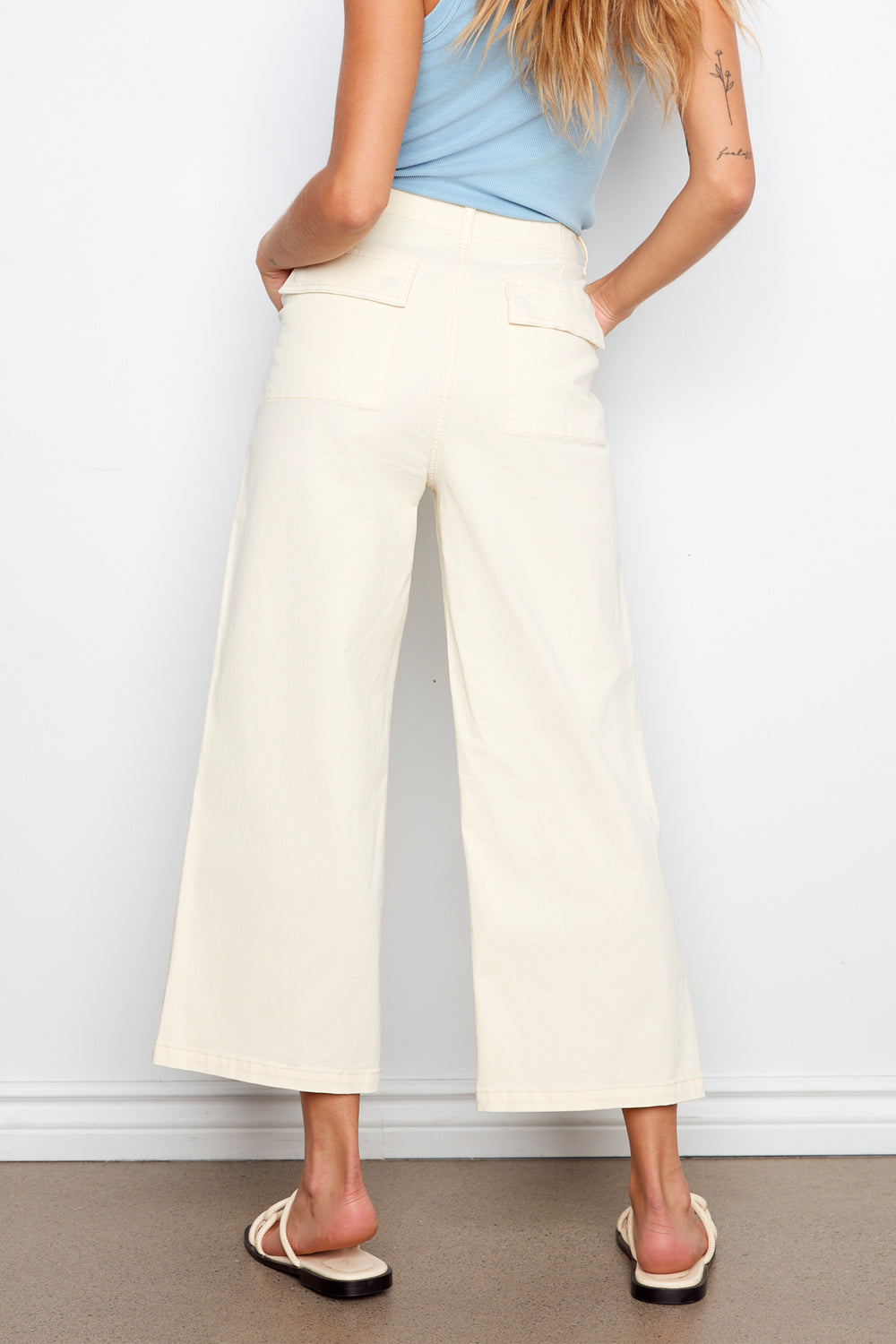 Person wearing white wide-leg pants and a light blue top against a plain background