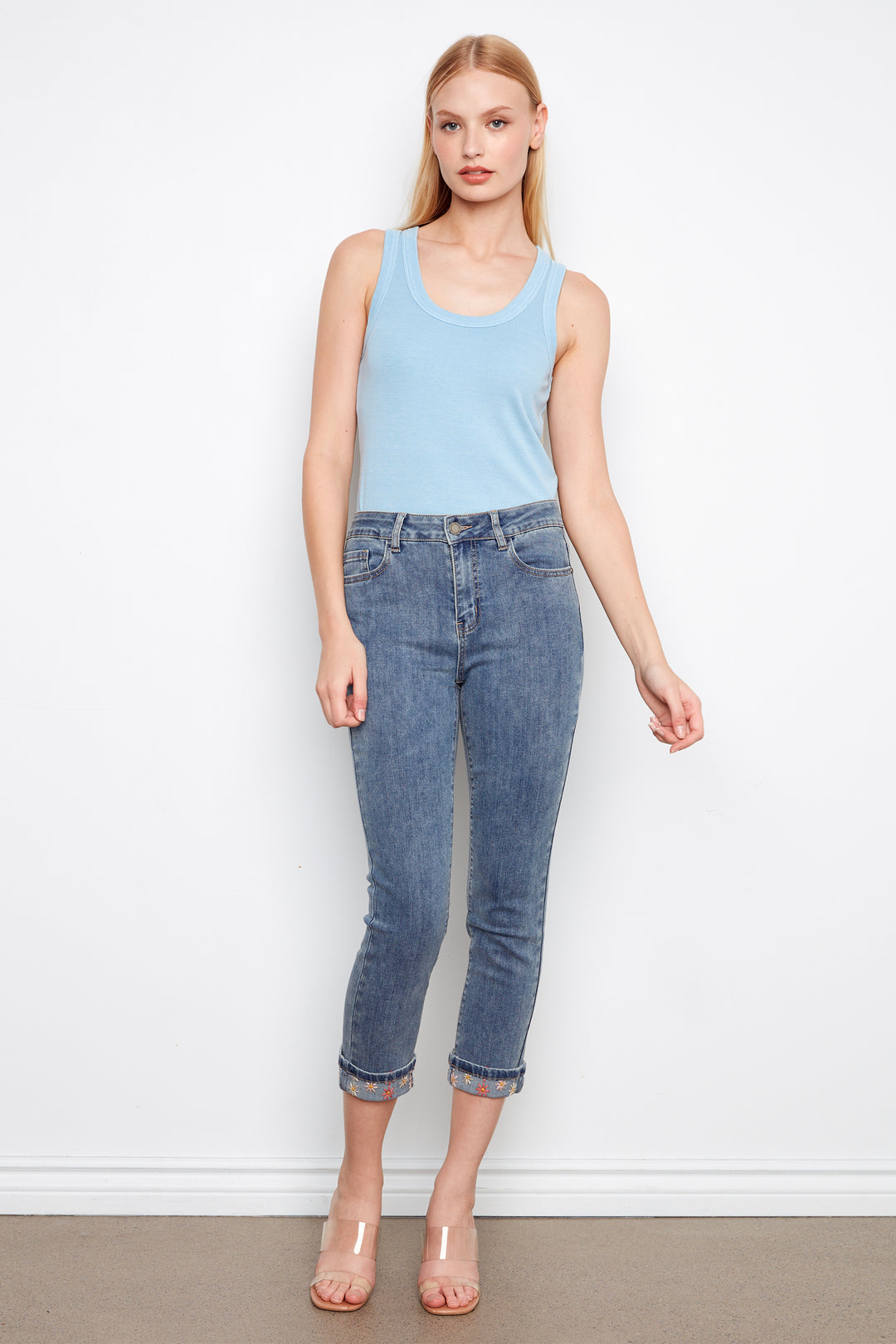 Woman wearing a light blue tank top and blue jeans against a white background