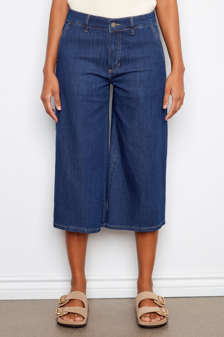 Person wearing blue denim culottes against a white background