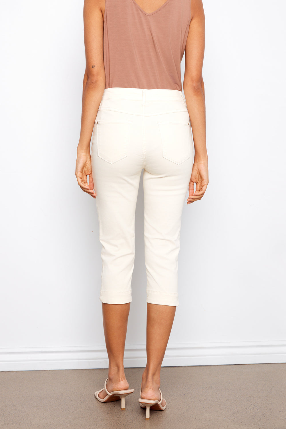 Person wearing a brown top and white capri pants against a white wall.