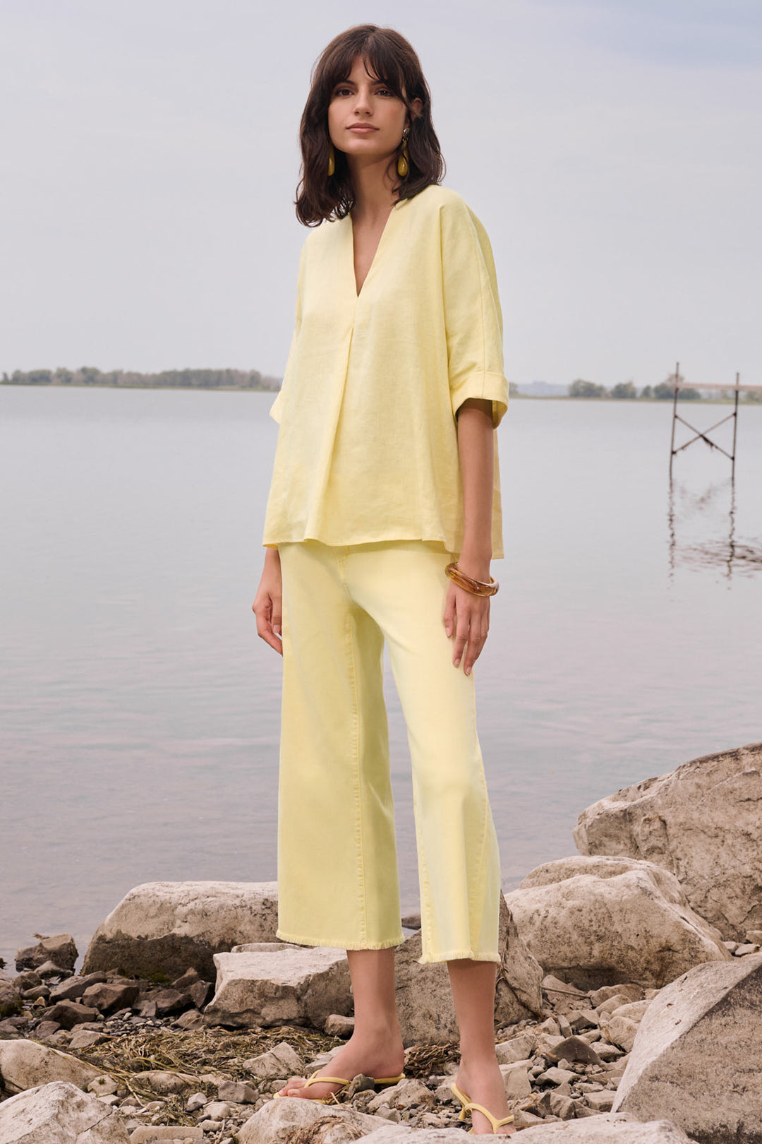 Woman in a yellow outfit standing by a body of water with rocks.