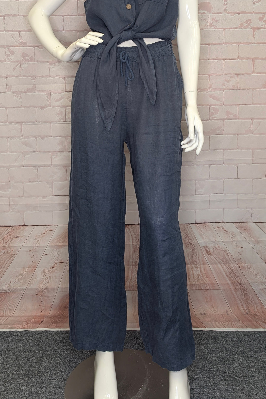 Mannequin wearing a dark blue linen pants against a brick wall.