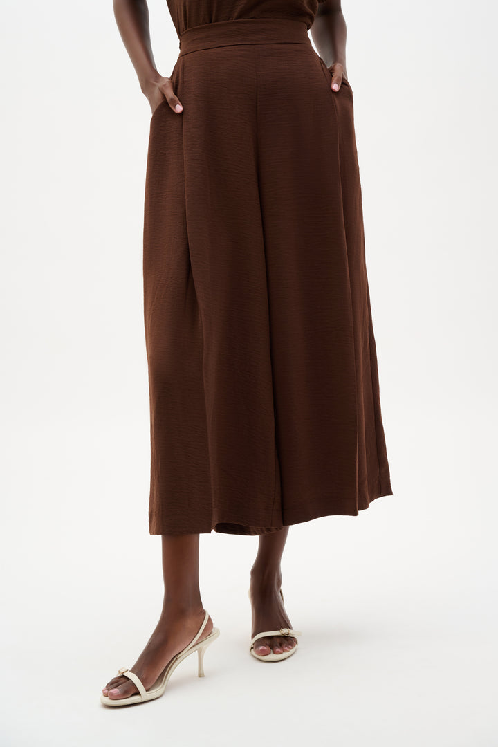 Person wearing a brown light dress with wide-leg pants on a white background