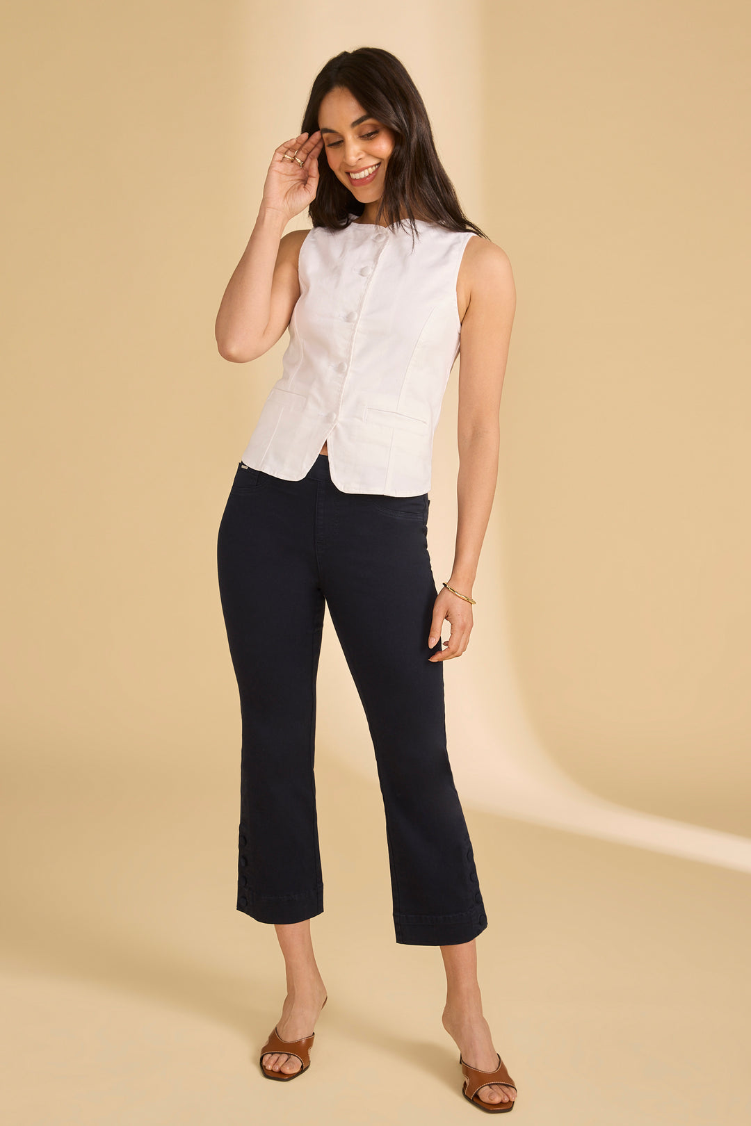 Woman wearing a white sleeveless top and black pants on a beige background