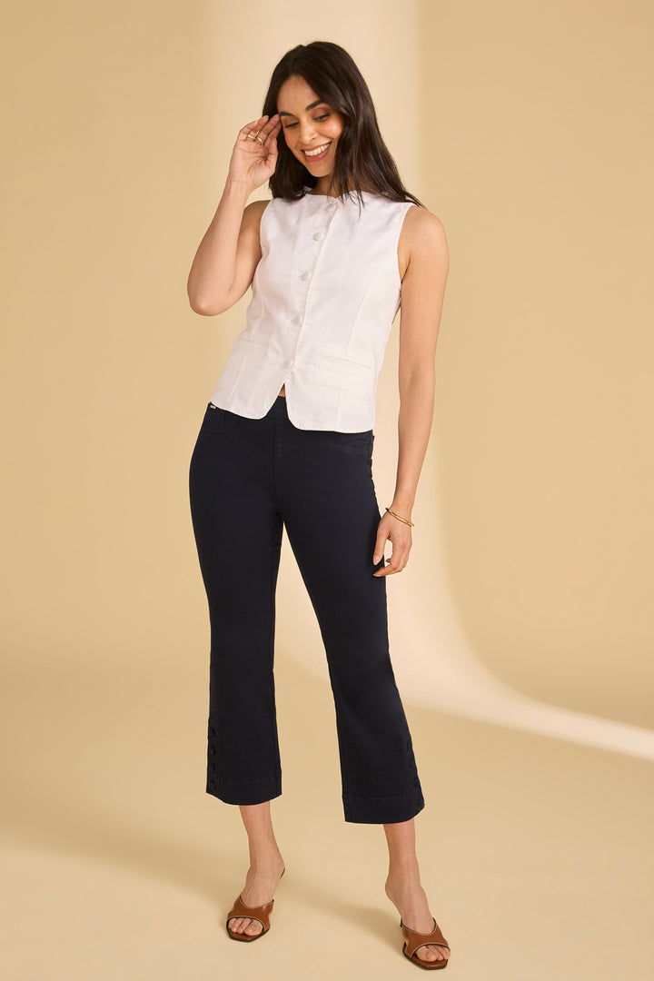 Woman wearing a white sleeveless top and black pants on a beige background